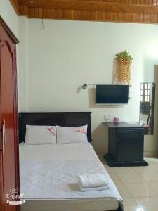 a bedroom with a bed and a tv on the wall at Hottel ANH LONG in Buôn Ðũng