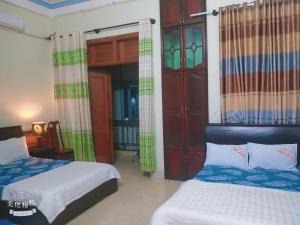 a bedroom with two beds and a door with curtains at Hottel ANH LONG in Buôn Ðũng