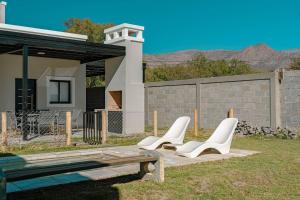 three white chairs and a bench in front of a house at Casa Tannat by Vindecaf in Cafayate