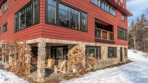 a red house in the snow with a bench in front of it at Luxe Vermont Duplex in Stowe