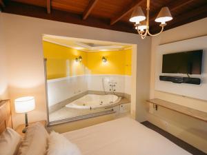 a bedroom with a tub with a bed and a television at Lê Château Hotel de Gramado, seu refúgio no centro da cidade in Gramado