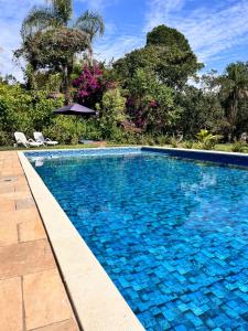 a blue swimming pool with two chairs and an umbrella at Villa Dona Jaca - Casa da Mata - 01 in Socorro