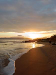 a sunset on a beach with people walking on the sand at Apartamento Castelhanos Anchieta in Anchieta