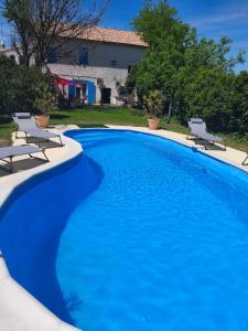 a large blue swimming pool with two chairs and a house at La maison d Adélaïde in Saint-Laurent-dʼAigouze