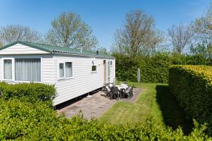 a white caravan with a table and chairs in a yard at chalet de kievit in Serooskerke