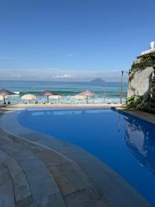 a swimming pool next to a beach with umbrellas at Juquehy La Plage Hotel in Juquei