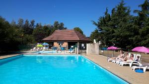 a swimming pool with people sitting on chairs and umbrellas at Camping de Saulieu in Saulieu