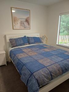 a bedroom with a bed with a blue checked comforter and a window at House in Restful Setting in Whangarei