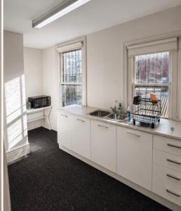 a white kitchen with a sink and two windows at Brunsi Hostel in Melbourne