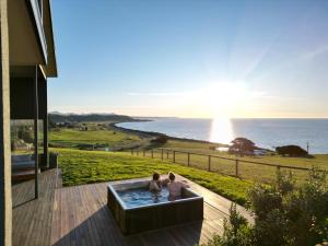 two people sitting in a hot tub on a deck with the ocean at The Cove Tasmania in Devonport