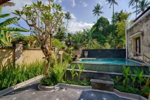 a swimming pool in a garden with a tree at Kubu Kapas Bali in Ubud