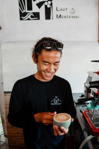 a man is smiling while holding a cup of coffee at Likat Surf House in Tua Pejat