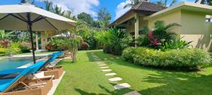 a yard with a pool and a house with an umbrella at TAMAN EDEN COTTAGE in Ubud