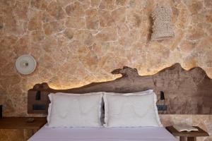a bed with two pillows in a room with a stone wall at Oikia Pouloudi in Kimolos