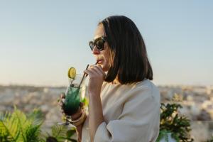 a woman drinking a drink with a city in the background at Royale Sainte Hélène Boutique Hotel in Birkirkara