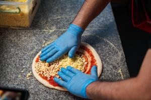 a person in blue gloves making a pizza on a counter at Argisht Partez Hotel ALL INCLUSIVE & BEACH BAR REBLS in Golden Sands