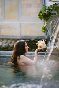 a woman in the water holding a plate of food at Puri Kantor Legacy - Heritage Palace in Ubud
