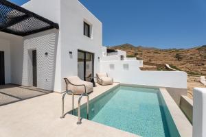 a white villa with a swimming pool with two chairs at Serenity Villas in Ios Chora