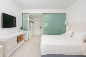 a white bedroom with a large bed and a tv at Dimitra Beach Hotel & Suites in Ágios Fokás