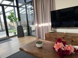 a living room with a television and a table with flowers at Luxus Chalet Visarend 13 Strandkristall in Hulshorst