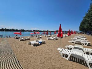 a beach with white chairs and red umbrellas at Apartman Dionis SM in Sremska Mitrovica