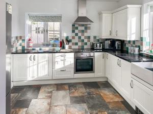 a kitchen with white cabinets and a tile floor at The Barn in Helston +14 photos