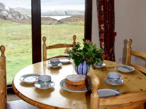 a wooden table with a cake and cups and a window at Orchid Cottage - Uk5866 in Achmelvich