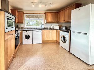 a kitchen with white appliances and wooden cabinets at Orchid Cottage - Uk5866 in Achmelvich +12 photos