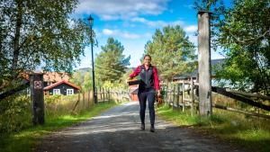 a woman walking down a dirt road near a fence at Søstrene Storaas hotell in Bolkesjø