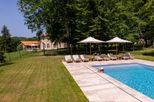 a swimming pool with chairs and umbrellas in a yard at Villa de La Roussie in Saint-Sulpice-de-Mareuil