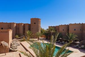 a view of a building with a pool and palm trees at Kasbah Hotel Tombouctou in Merzouga