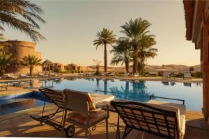 a swimming pool with two chairs and palm trees at Kasbah Hotel Tombouctou in Merzouga