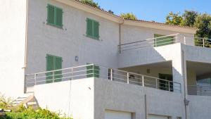 a white building with green windows and a balcony at Maison confortable avec vue sur la mer et la montagne à Oletta. in Oletta