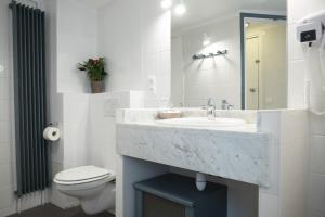a white bathroom with a sink and a toilet at Hôtel du Cygne Paris in Paris