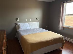 a bedroom with a bed with a yellow blanket and a window at The Sunshine Inn in Parrsboro