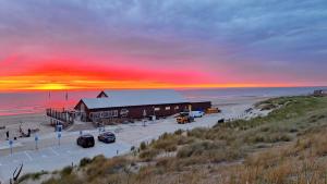 a building on the beach with a sunset in the background at De Strandloper in Petten