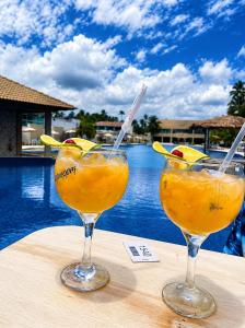 two glasses of orange juice on a table next to a pool at Hotel Maragogi Beach Club in Maragogi