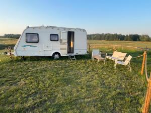 a white caravan in a field with chairs and a table at Weź Wyjdź - Podlaski Glamping in Łazy +27 photos