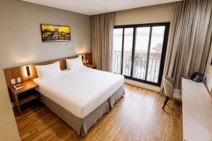 a hotel room with a large bed and a large window at Royal Tulip Holambra in Holambra