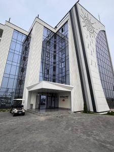 a large building with a car parked in front of it at Raduga West Apart Hotel in Koshkolʼ
