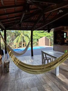 a hammock on a patio with a table and a pool at Encanto na Mata in Mata de Sao Joao