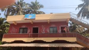 a red building with a balcony and palm trees at Heera BEACH WAVE STAY in Gokarn