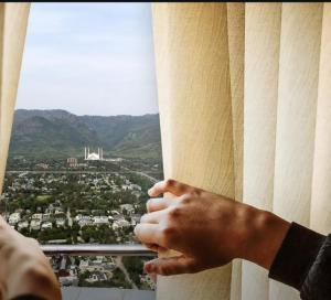 a persons hand looking out a window at a city at AH apartments in Rawalpindi