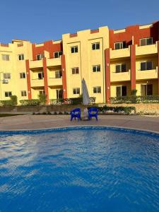 a swimming pool with two blue chairs in front of a building at لاسيرينا عيون موسى LaSerinaللعائلات in Ras Sedr +5 photos