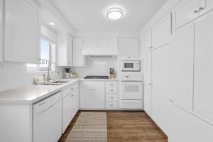 a white kitchen with white appliances and a wooden floor at Newport Coastal Charm in Newport Beach +16 photos