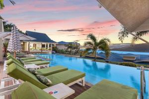 a swimming pool with green lounge chairs next to a house at Club Airlie in Airlie Beach