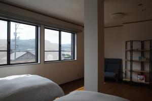 a bedroom with two beds and windows and a chair at はなれ香 in Kirishima