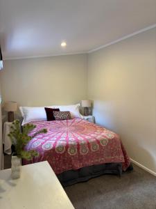 a bedroom with a bed with a red comforter at Lulu's Cottage by Native Forest in Waimauku