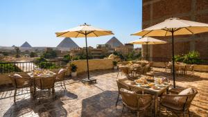 a patio with tables and umbrellas with pyramids in the background at House Pyramids View Hotel in Cairo