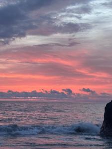 a sunset over the ocean with rocks in the water at Hotel GinaMar Ladrilleros in Buenaventura